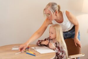 Math Parent: lady pointing to object on table, little girl sitting at the table.
